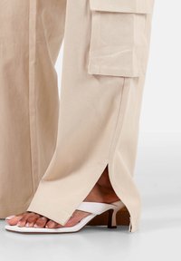 Beige wijde broek met een zijsplit en zakdetails, gecombineerd met witte hakken met een minimalistisch bandontwerp.