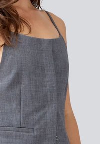 Top sans manches en lin gris présentant un décolleté carré, des coutures détaillées et une poche avant avec une texture subtile.