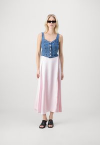 Farmerekből készült cropped top, gombos elejével és vékony pántokkal, amelyet egy hosszú, sima rózsaszín selyem szoknyával és fekete nyitott orrú mamuszokkal párosítanak.