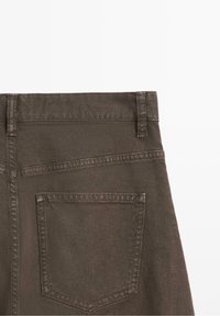 Vue arrière d'un pantalon en denim marron montrant la ceinture, les passants de ceinture et une seule poche arrière avec des coutures visibles.