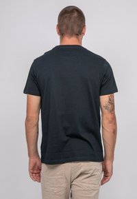 T-shirt en coton noir à manches courtes, col rond et coupe droite, vu de l'arrière. Présenté sur un fond neutre.
