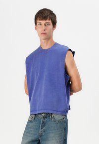 Lila ärmelloses Sweatshirt mit klassischem Rundhalsausschnitt, weichem Textil, tiefen Armöffnungen und lockerer Passform, kombiniert mit ausgewaschenen blauen Jeans.