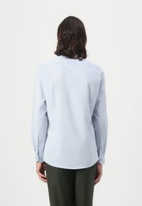 Light blue long-sleeve shirt with a fitted design, button cuffs, and a back yoke. Smooth texture with a subtle sheen.