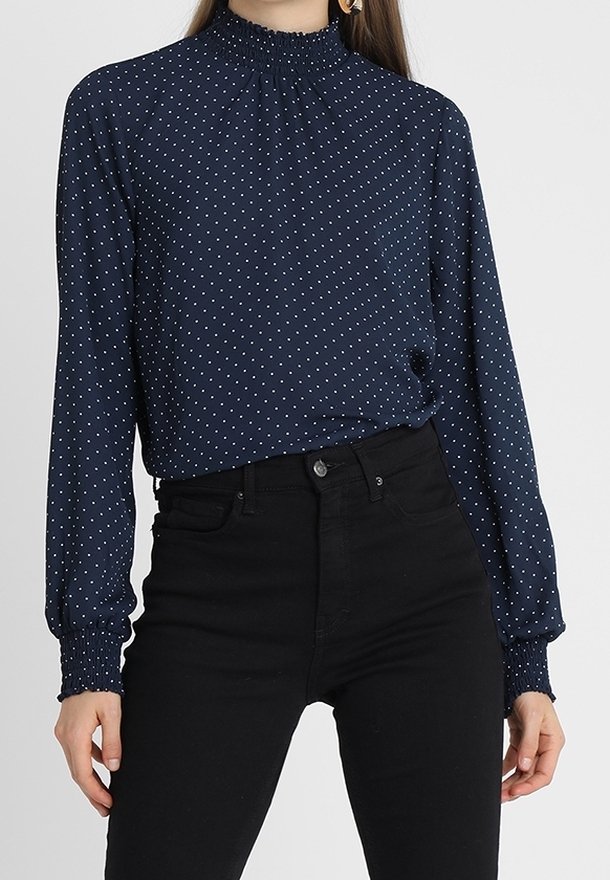 Marinblus med prickar, långärmad och med hög smockad krage, med en slät textur och elastiska ärmslut, matchad med svarta jeans.
