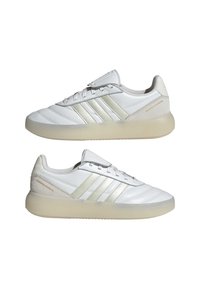 Paire de baskets Adidas Barreda Mundial blanches avec semelles translucides et trois bandes beige clair sur les côtés, présentées de profil gauche.