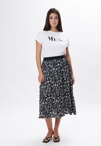 Hvid T-shirt med sort "Muse" tekst, parret med en sort blomsterkjole med hvide blomster. Sorte strop sandaler fuldender looket.