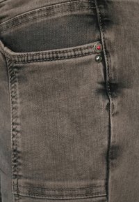 Šedé džíny z denimu s texturovanou tkaninou, designem s pěti kapsami a dvěma dekorativními kovovými knoflíky s červeným akcentem.