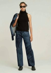 Must have mustata selja turtleneck, sinise mustriga laiad püksid ja teksajakk. Modell kannab musti päikeseprille ja massiivseid musti kingi.