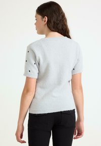 Lys grå kortærmet sweater med en blød tekstur, der har sorte stjerne accenter på ærmerne og en ribbet kant.