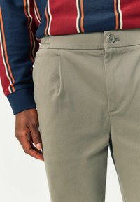 Light gray trousers feature side pockets, a button closure, and a smooth texture. A navy striped long-sleeve shirt is worn above.