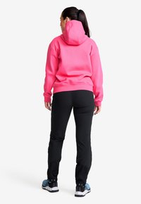 Rosa huvtröja, svarta byxor och blåa sportskor. Har en avslappnad passform, ribbade muddar och snörning i huvan.