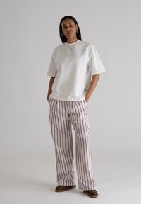 White cotton t-shirt with short sleeves, paired with wide leg striped pants in red and white. Brown shoes complete the outfit.