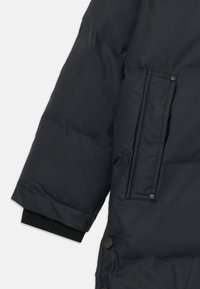 Secção de casaco puffer preto com um tecido liso e texturizado, um bolso lateral com fecho de botão de pressão e um punho preto canelado.