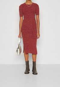 Rotes, geripptes Strickkleid mit kurzen Ärmeln und seitlichem Schlitz, kombiniert mit grauen Knöchelstiefeln und einer silbernen Handtasche. Glatte Textur, figurbetonter Schnitt.