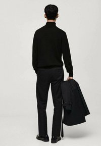 Svart tröja med hög krage, kombinerad med mörka byxor. Håller en svart jacka. Slät tyg, minimalistisk design.