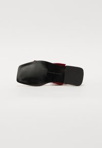 Black leather sandal with a square toe and textured sole. Features a bold red strap across the upper and a flat sole design.