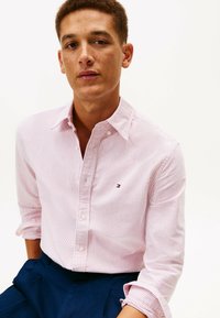 Maglietta a maniche lunghe a righe rosa chiaro e bianco, realizzata in cotone. Presenta un colletto con bottoni e un logo discreto sul petto.