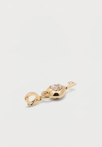 Γούρι σε σχήμα χρυσού κλειδιού με καθαρό πολύτιμο λίθο κομμένο σε σχήμα καρδιάς και μικρούς στρογγυλούς κρυστάλλους, προσαρτημένο σε κυκλικό κούμπωμα.