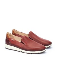 Zapatillas rojas sin cordones de cuero perforado, con un acento en el tacón color marrón, suela blanca y un diseño aerodinámico que facilita su uso.