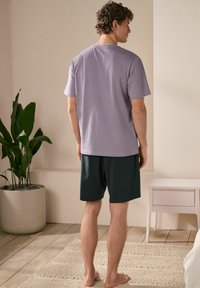 Lila kortärmad t-shirt, avslappnad passform, i kombination med mörkgröna shorts. Slät bomullsmaterial med en enkel design. Inga synliga mönster eller logotyper.