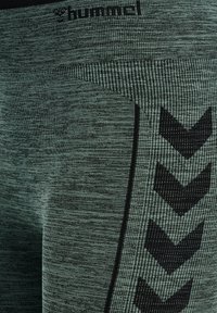 Zielone legginsy o fakturze z delikatnym wzorem, z czarnym wzorem chevron wzdłuż boku oraz logo marki na pasku talii.