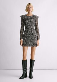 Vestido mini de estampado floral con mangas largas abullonadas, diseño fruncido y silueta ajustada, combinado con botas de cuero negras hasta la rodilla.