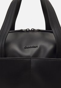 Borsa a tracolla in pelle nera con zip, design minimalista e logo impresso. Presenta manici larghi e una texture liscia.