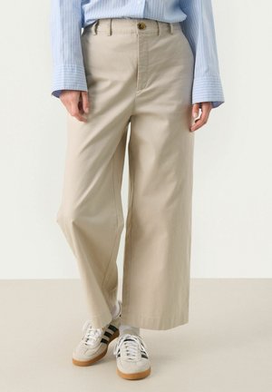 Beige wide-leg trousers with a high waist, front button detail, and soft texture, paired with light-colored sneakers with black stripes.