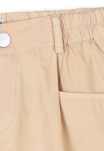 Shorts beige avec une taille élastique, une fermeture à bouton et une petite poche latérale. Présente des coutures visibles et une texture de tissu lisse.