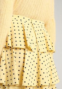 Gonna gialla a più strati con pois neri abbinata a un maglione lavorato a maglia giallo testurizzato.