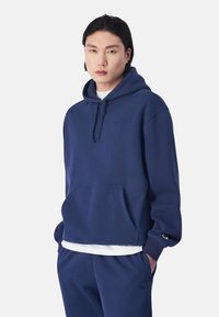 Dunkelblauer Hoodie aus weichem Stoff mit einer Vorderseite-Tasche, Kordelzugkapuze und gesticktem Logo auf der Brust. Hat einen lässigen Schnitt.