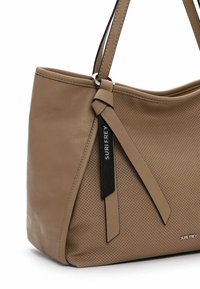 Bolso de cuero topo con frente perforado, asas dobles y lazos decorativos en negro y topo, con etiqueta metálica de la marca "SURI FREY".