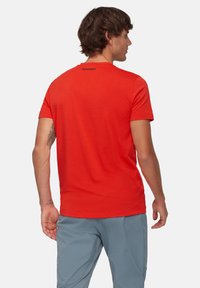 Röd t-shirt med kort ärm gjord av lättviktsmaterial, med rundad halsringning och en liten svart logotyp på baksidan. Slät textur.