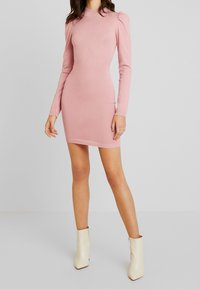 Robe moulante rose à manches longues avec poignets et ourlet côtelés. Dotée de détails à épaules bouffantes, en tissu doux, associée à des bottines blanches à la cheville.