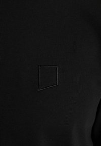 Crna pamučna dukserica s teksturiranim, izvezenim geometrijskim dizajnom u gornjem lijevom kutu. Glatka, elastična tkanina s prilagođenim oblikom.