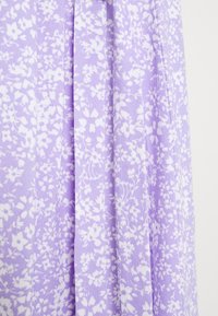 Tissu violet clair avec un motif floral blanc. La texture semble douce, avec des plis créant des drapés dans le matériau.