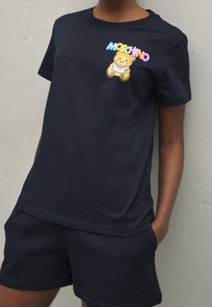T-shirt en coton noir avec un logo "Moschino" coloré et un graphisme de ours en cartoon sur la poitrine gauche. Manches courtes, col rond.