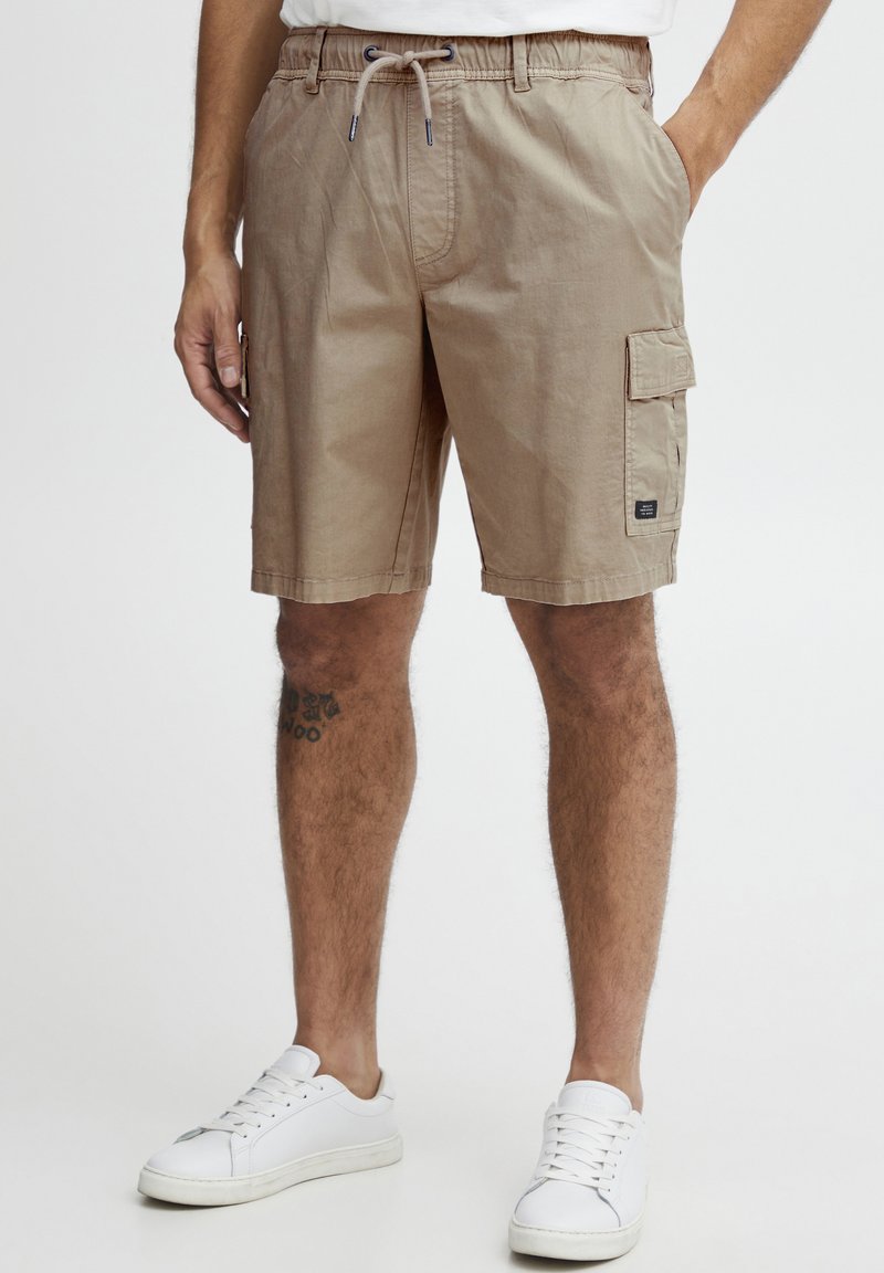 Pantalones cortos de cargo beige, hechos de algodón, con una cinturilla elástica, cordón ajustable y un bolsillo lateral tipo cargo.
