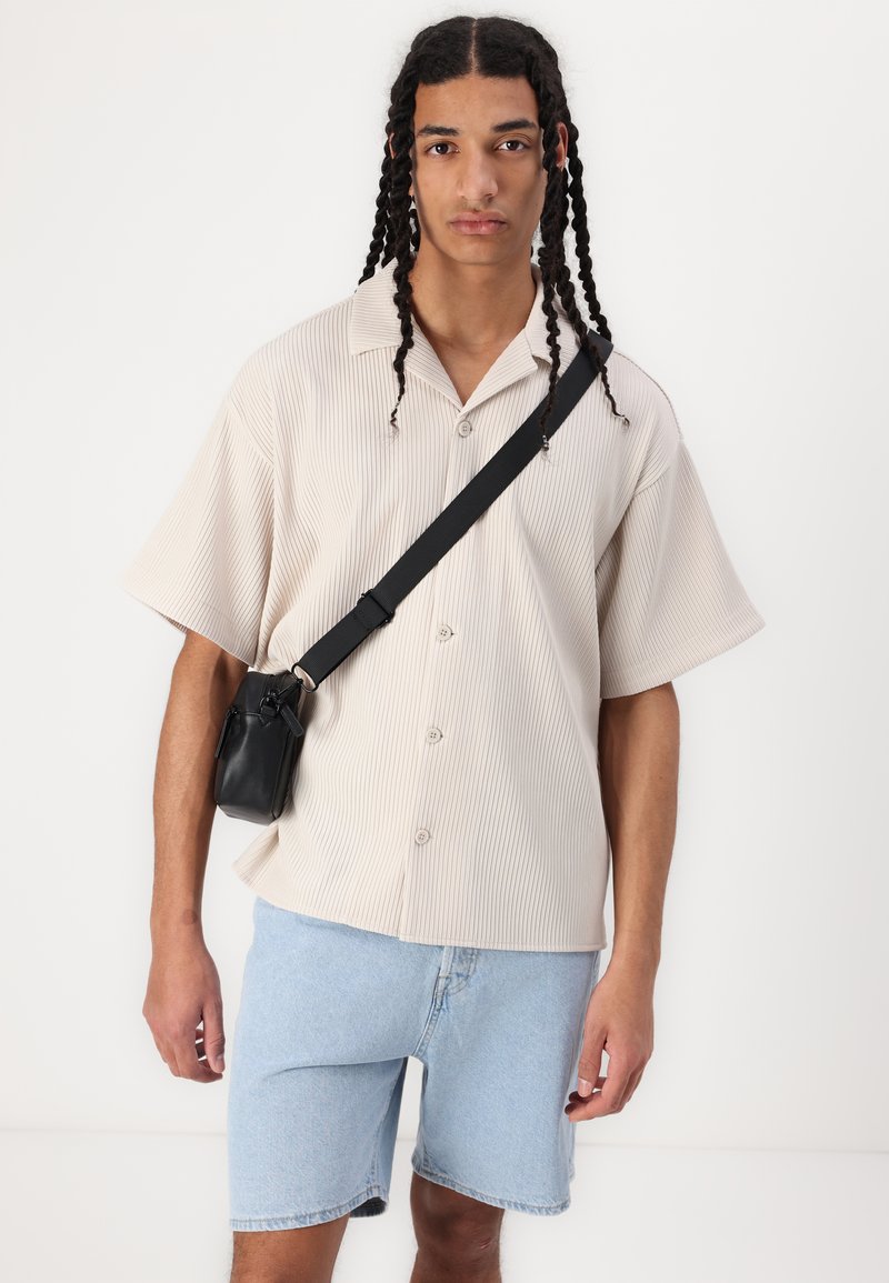 Koszula z krótkim rękawem w beżowe paski, luźny krój, w połączeniu z jasnoniebieskimi szortami dżinsowymi i małą czarną torebką na ramię.