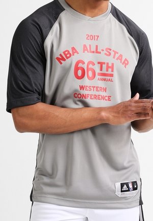 Man draagt een grijs-zwart Adidas NBA All-Star 2017 Western Conference 66e jaarlijkse shirt, met handen samengevouwen voor zich.