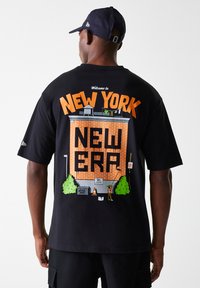 Maglietta nera a maniche corte con una grafica di un edificio in mattoni, con "BENVENUTO A NEW YORK" e "NEW ERA" in arancione, illustrazioni colorate sottostanti.