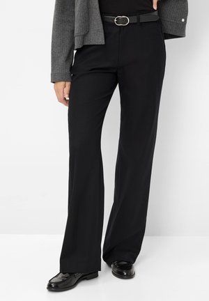 Pantalons larges noirs en tissu lisse, dotés d'une taille haute et d'une ceinture avec une boucle en argent ronde. Associés à des chaussures noires brillantes.