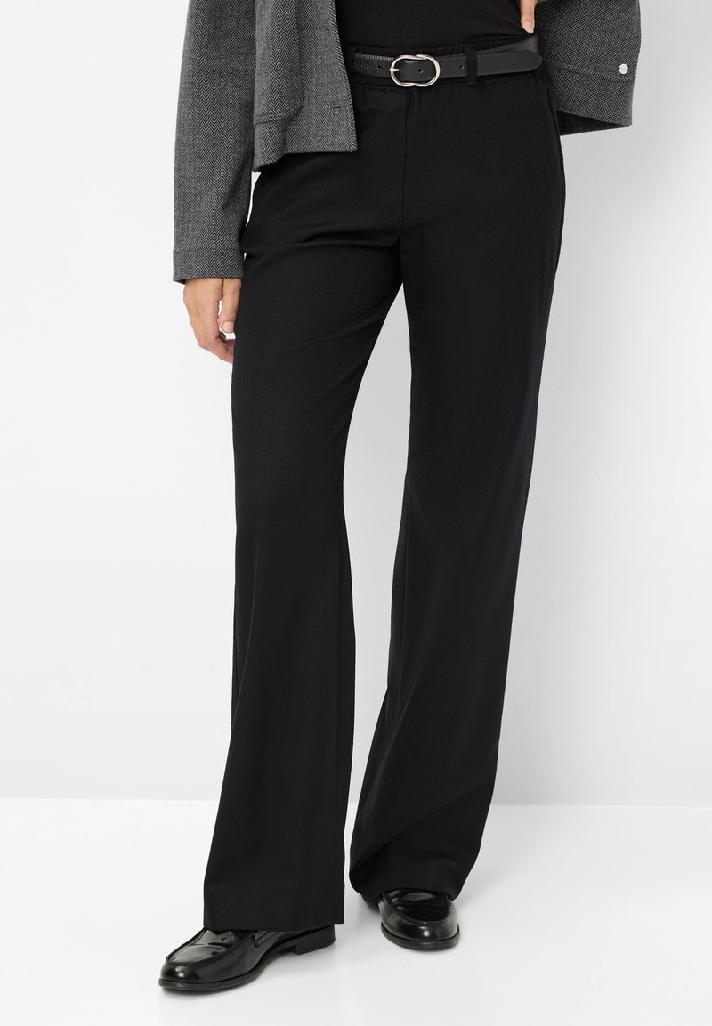 Pantalons larges noirs en tissu lisse, dotés d'une taille haute et d'une ceinture avec une boucle en argent ronde. Associés à des chaussures noires brillantes.