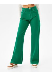 Gröna vida jeans med kontrasterande sömmar, hög midja och framfickor. Kombinerat med vita och bruna sneakers.