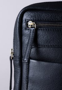 Black leather bag featuring a textured surface, gold zipper hardware, and a slim, rectangular shape with stitched accents.
