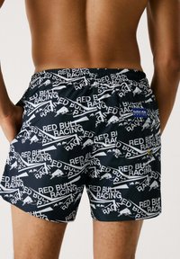 Bañador negro con un diseño repetido en blanco del logo y la silueta de "Red Bull Racing". Cintura elástica con detalle de bolsillo trasero.