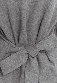 Top in tessuto grigio con nodo dietro. Tessuto morbido e forma ampia con maniche lunghe. Design semplice senza motivi o dettagli.