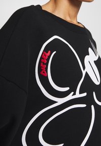 Sudadera negra con un gran diseño gráfico blanco y el logo rojo "DIESEL" en el lado izquierdo. Textura suave, estilo con cuello redondo.