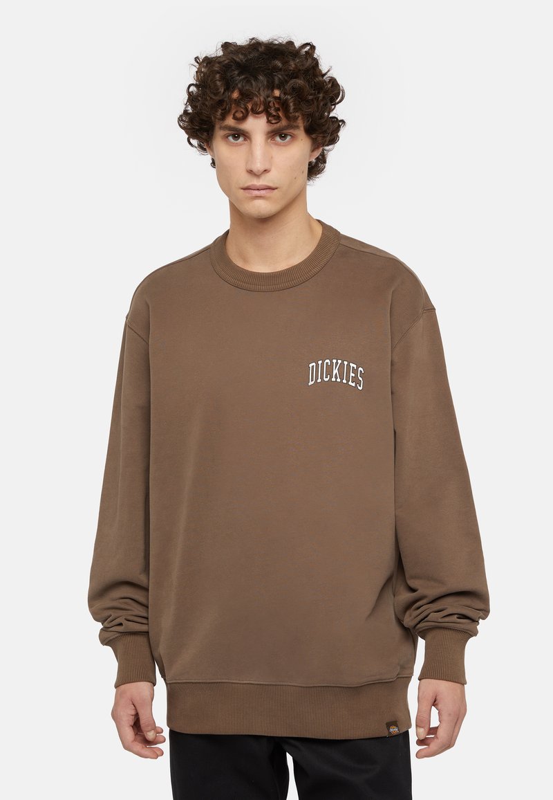 Sudadera marrón con cuello y puños de canalé. Incluye el logo blanco "DICKIES" en el pecho. Tela suave, corte relajado y una etiqueta en la parte inferior.