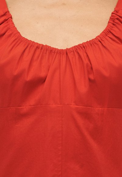 Κοντινό πλάνο λαιμού κόκκινης φόρεμα με ραμμένη ελαστική τρέσα και ορατές ραφές σε λείο ύφασμα.